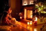 Kerstkaart: Moeder zit met twee dochters voor de open haard waar ook brandende kaarsen voor staan